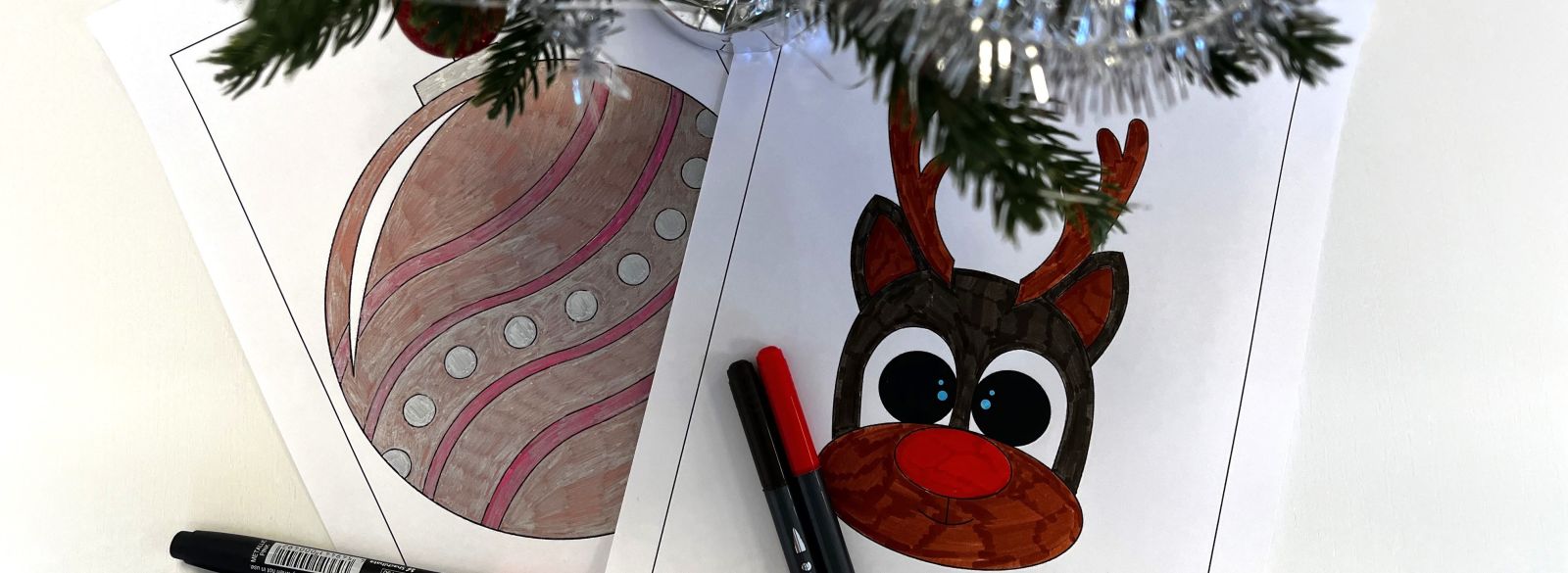 Julpyssel med målarbilder, färglagda teckningar av en julkula och en ren, tillsammans med färgpennor och en grankvist med silverglitter.